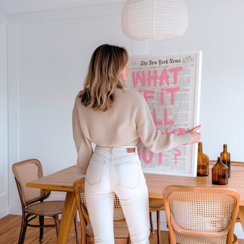 Puede incluir: Un su&eacute;ter beige de manga larga acanalado y pantalones vaqueros blancos. Un cuadro enmarcado muestra el texto The New York News con las palabras WHAT IF IT ALL WORKS OUT? en letras rosas grandes. Tres botellas de vidrio &aacute;mbar sobre una mesa de madera.