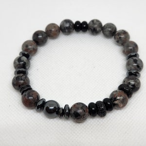 May include: A black and gray beaded bracelet with black and silver accents. The bracelet is made of round beads with a speckled pattern.