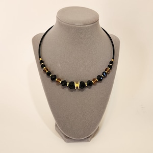 May include: A black and gold beaded choker necklace with a gold accent piece in the centre.
