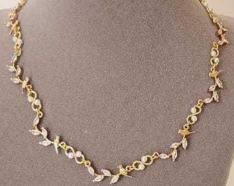 May include: A gold necklace with a delicate design featuring small leaves and pearl accents. The necklace is on a gray mannequin bust.