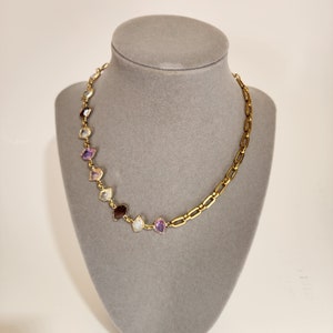 Pode incluir: Um colar de corrente de ouro com uma fileira de pedras preciosas coloridas. As pedras preciosas são engastadas em ouro e estão dispostas em um degradê de roxo para vermelho. A corrente é uma corrente simples e ligada.