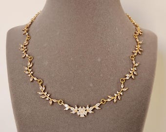 May include: A gold necklace with a delicate design of leaves and flowers, adorned with clear cubic zirconia stones.