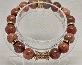 May include: A brown gemstone bracelet with gold accents and a gold and clear crystal bead in the centre.