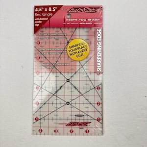 Puede incluir: Regla de acolchado rectangular transparente, 11,4 cm x 21,6 cm, con borde de polvo de diamante. Cuenta con un sistema de cuadrícula, ángulos diagonales y el texto "SHARPENS YOUR BLADE WITH EVERY CUT!" y "SHARPENING EDGE".