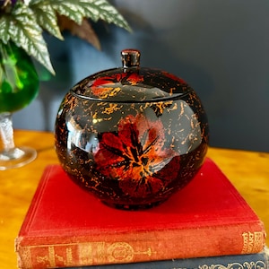 May include: A white ceramic mug with a black handle and the text "But First, Coffee" in a bold, black font. The mug is set against a blurred background, suggesting a cosy setting.