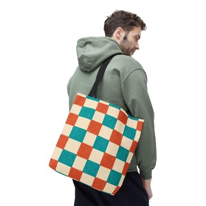 May include: A canvas tote bag with a black strap and a colorful checkerboard pattern. The pattern features alternating squares of cream, teal, and orange. The bag is carried over the shoulder.