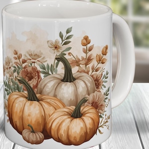 Puede incluir: Taza de cerámica blanca con un diseño otoñal. El diseño presenta calabazas naranjas y elementos florales otoñales en tonos marrón, beige y verde. La taza tiene un asa blanca y un acabado brillante.