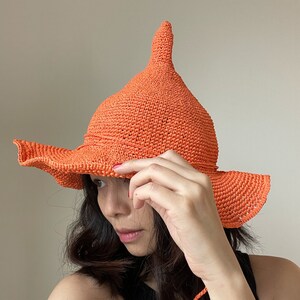 May include: A bright orange crochet sun hat with a pointed crown and wide brim. The hat is made of a fine, textured yarn and has a simple, elegant design.