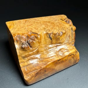 May include: A small, intricately carved wooden box with a natural wood finish. The box has a unique, irregular shape and a textured surface.