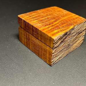 May include: A small, wooden box with a lid. The box is made of two pieces of wood, one on top of the other. The wood has a reddish-brown color and a natural grain pattern.