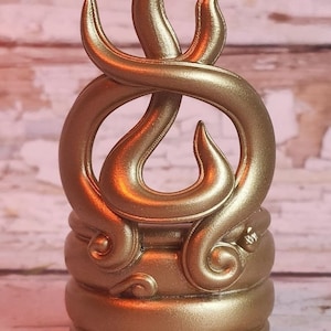May include: A gold-colored, decorative, 3D printed flame-shaped bottle stopper. The flame is intricately designed with a swirling pattern and sits on a round base.