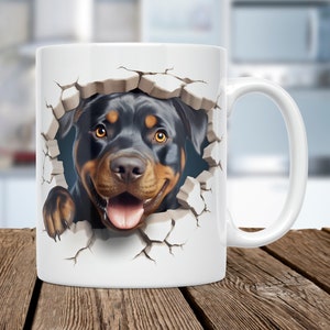 May include: White ceramic mug with a graphic of a Rottweiler dog's head peeking through a cracked wall. The dog has black fur, brown eyes, and a pink tongue sticking out.