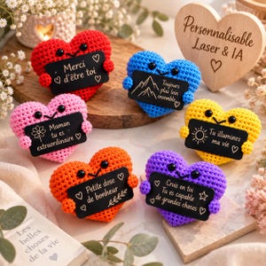 Peut inclure: Six cœurs crochetés en rouge, bleu, rose, jaune, orange et violet, chacun avec des yeux noirs et tenant un petit panneau rectangulaire noir avec du texte blanc en français et des icônes, incluant Merci d'être toi et Tu illumines ma vie.