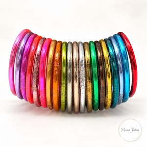 Pode incluir: Uma coleção de dezoito pulseiras circulares finas dispostas em fila, apresentando um acabamento metálico reflexivo num espectro de cores incluindo rosa, laranja, amarelo, verde, prata, ouro, castanho, azul e vermelho, com o texto Maison Yvelise.