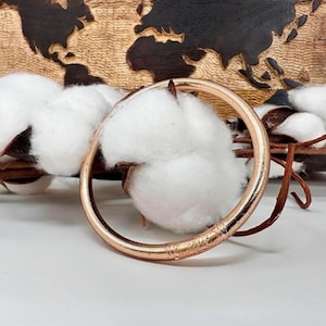 Pode incluir: Um bracelete de ouro rosa com um design texturizado. O bracelete está sobre uma superfície branca.