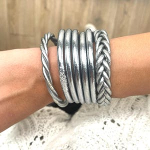 Peut inclure: Plusieurs bracelets argentés sur un poignet. Les bracelets comprennent un design torsadé, plusieurs bandes lisses et un style tressé. Les bijoux sont en matériau métallique brillant. Les bracelets sont empilés pour un look superposé.
