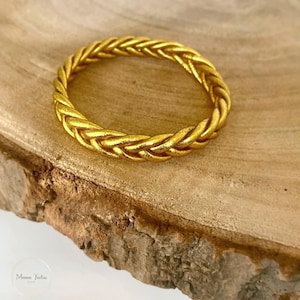May include: A gold braided bangle bracelet. The bracelet is made of a thick, braided metal and has a shiny finish.