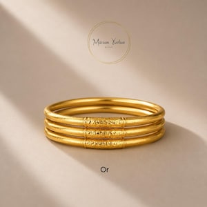 Può includere: Tre braccialetti d'oro impilati. Ogni braccialetto ha un design liscio e arrotondato con dettagli strutturati al centro. La parola "Or" è in basso nell'immagine. Il marchio "Maison Yvelise Bijoux" è in alto.