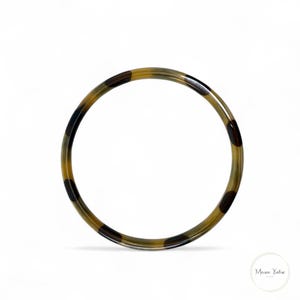 May include: A circular bangle bracelet with a tortoiseshell pattern. The bracelet features a mix of brown, black, and tan colors. The bangle is made of a smooth, glossy material and is set against a white background.