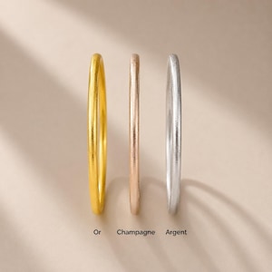 Peut inclure: Trois fines bagues en or, champagne et argent. La bague en or est à gauche, la bague champagne au milieu et la bague argent à droite. Les mots "Or", "Champagne" et "Argent" sont écrits sous chaque bague.