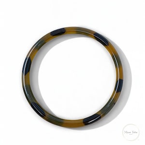 Peut inclure: Un bracelet jonc à motif brun et noir. Le bracelet est en résine et a une finition brillante.