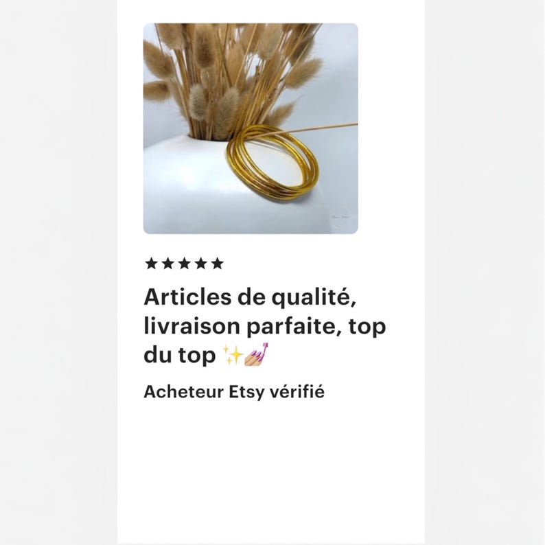 May include: A white ceramic vase holds dried, tan-colored ornamental grass. Several gold-colored bangles are stacked in a circular arrangement. The image also includes text in French: "Articles de qualit&eacute;, livraison parfaite, top du top".