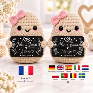 Könnte beinhalten: Zwei beige gehäkelte Kartoffelpuppen mit rosa Schleifen, schwarzen Augen und rosa Wangen. Jede hält ein schwarzes rechteckiges Schild mit weißem Text und Blumenmotiven. Die Schilder zeigen die Namen Jules & Jeanne sowie Alex & Emma mit Datum.