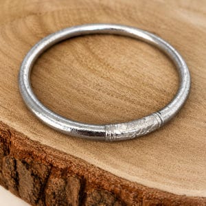 May include: A silver bangle bracelet with a detailed floral pattern. The bracelet is round and has a smooth, polished finish. The bracelet is displayed on a wooden surface.
