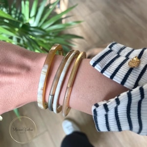 Peut inclure: Quatre bracelets empilés sur un poignet. Les bracelets sont en corne et ont une couleur naturelle brun et blanc. Le bracelet du haut a un accent doré.