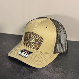 May include: Tan and black trucker hat with the text "MY WIFE WILL KILL YOU" on a brown patch. The hat has a curved brim and a mesh back. The hat is adjustable and has a Richardson 112 tag.