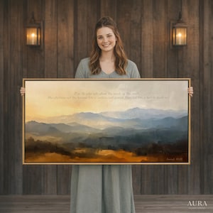 Puede incluir: Pintura de paisaje enmarcada con una escena de cordillera en tonos azules, marrones y amarillos. La obra de arte presenta texto de Isaías 40:22. La pintura es sostenida por una persona frente a una pared de madera.