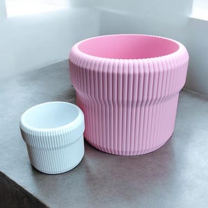 May include: Two ribbed plastic planters, one pink and one white. The pink planter is larger than the white planter.