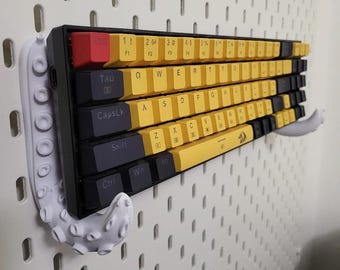 May include: A white octopus-shaped keyboard holder mounted on a pegboard wall. The keyboard is black with yellow keys and has the numbers 1 through 5 and the letters F1 through F5 printed on the keys.