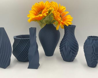 May include: Five blue ceramic vases with different textured patterns. The vases are arranged on a white surface with a bouquet of yellow sunflowers in the center.