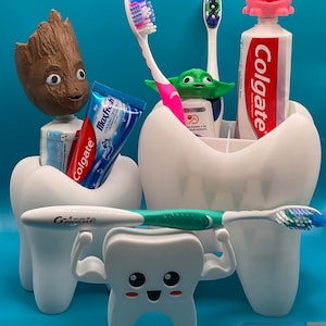 Peut inclure: Ensemble de porte-brosses à dents et de distributeurs de dentifrice originaux en forme de dents. Les supports présentent des personnages comme Groot, Yoda et un cochon. Des brosses à dents et des tubes de dentifrice sont affichés dans les supports.