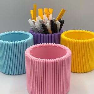 Può includere: Tre contenitori cilindrici con una texture a coste. I contenitori sono azzurro, rosa e giallo. Il contenitore azzurro è a sinistra, il contenitore rosa è al centro e il contenitore giallo è a destra. I contenitori sono vuoti.