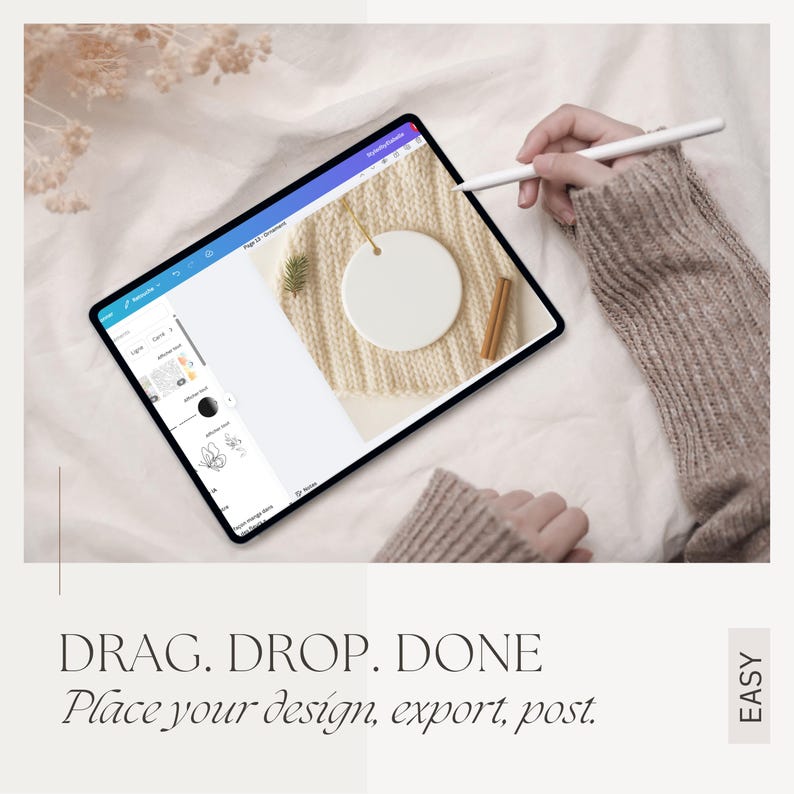 May include: A digital tablet displaying a design interface with a blank white ornament. The tablet is on a cream-colored knitted surface with a sprig of greenery and a cinnamon stick. Text reads: DRAG. DROP. DONE. Place your design, export, post.