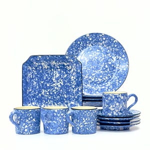 May include: A complete blue and white speckled stoneware dinnerware set. The set includes plates, saucers, mugs, and a square serving dish. The rims of the mugs and serving dish are outlined in black.
