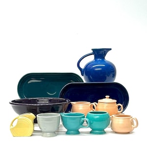 May include: A collection of colorful ceramic tableware in various shapes and sizes. Includes serving platters, bowls, pitchers, sugar bowls, and mugs in shades of blue, teal, yellow, peach, and gray. The pieces are arranged on a white background.
