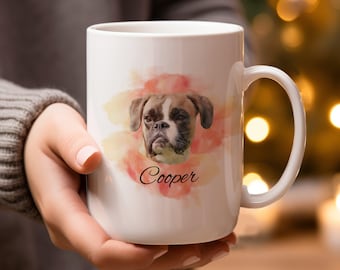 May include: White ceramic mug featuring a Boxer dog portrait with the name "Cooper" in script. The dog's image is set against a watercolor-style background of pink and yellow hues. The mug has a large handle.