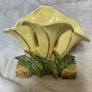 Peut inclure: Un vase en céramique jaune en forme de fleur stylisée avec des feuilles vertes et une base brune.