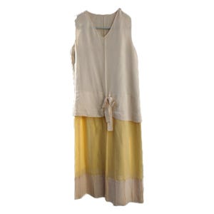 Peut inclure: Robe sans manches avec un col en V. Le haut est beige clair, le bas jaune avec un ourlet beige. Un détail de nœud est à la taille. La robe est suspendue à un cintre gris. Idéale pour l'été.