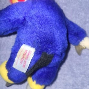 May include: A plush Woody Woodpecker toy, primarily blue with a red head and yellow feet. The toy has a black tail and a white tag that reads "Hanging Woody Woodpecker."