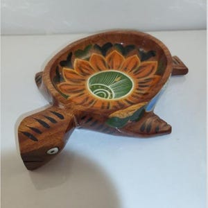 May include: A wooden turtle-shaped bowl with a painted sunflower design. The bowl is painted in shades of brown, orange, green, and blue.