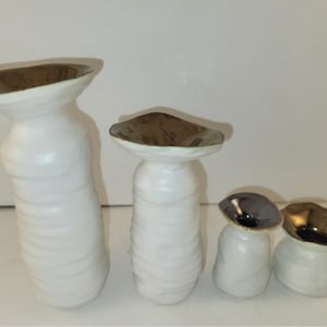 May include: Set of four white ceramic vases with gold rims. The vases are of varying sizes and have a textured, wavy design.