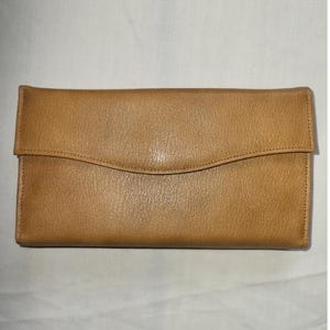 May include: A tan leather wallet with a curved flap closure. The wallet is rectangular and appears to be made of a smooth, durable material. The flap has a subtle, curved design, adding a touch of elegance to the accessory.
