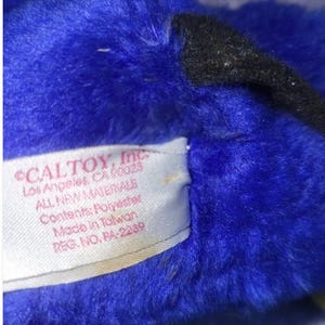 May include: Close-up of a plush toy with vibrant blue fur and a black accent. A tag reads "CALTOY, Inc. Los Angeles, CA 90023 ALL NEW MATERIALS Contents: Polyester Made in Taiwan REG. NO. RA-2239".