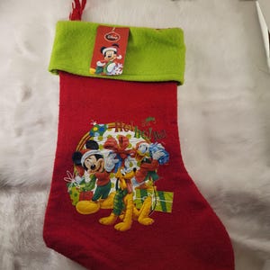 May include: Red Christmas stocking with a green cuff and a red loop for hanging. The stocking features Mickey Mouse, Donald Duck, and Pluto with wrapped gifts. The text "Ho Ho Ho!" is also visible.