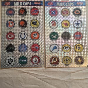 May include: Two sheets of collectible milk caps featuring various NFL team logos. The caps are round with team colors and logos, set against a silver, textured background. The text "MILK CAPS" is printed at the top of each sheet.