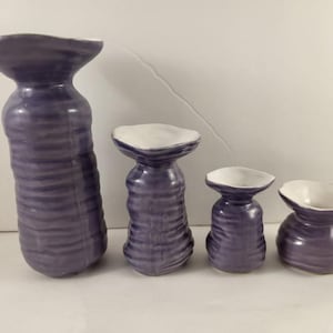 May include: Set of four purple and white ceramic vases with a wavy texture. The vases are different sizes and shapes.